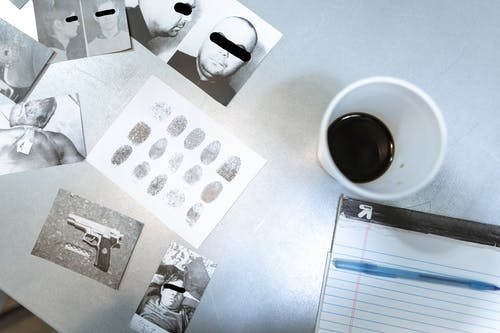 Pictures and fingerprints from a crime scene lying next to a coffee cup and notebook