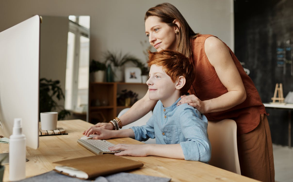 A woman helping a child with research on a computer 