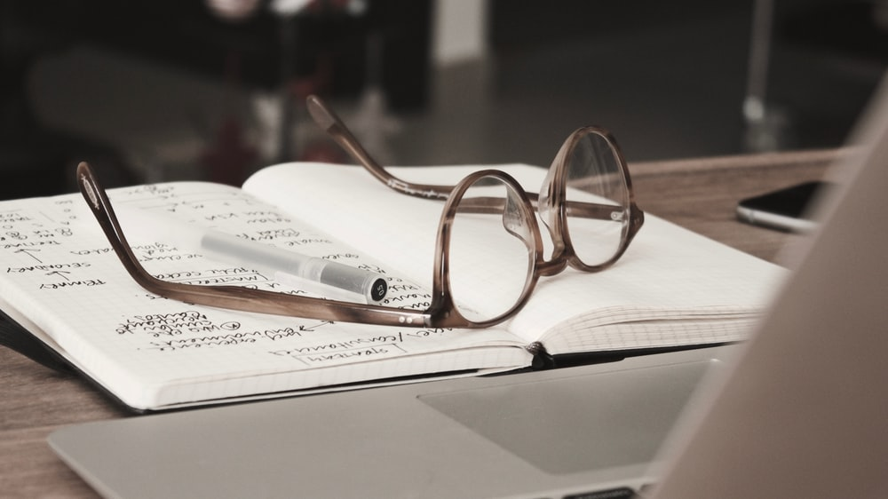 glasses lying on top of an open notebook near a laptop 