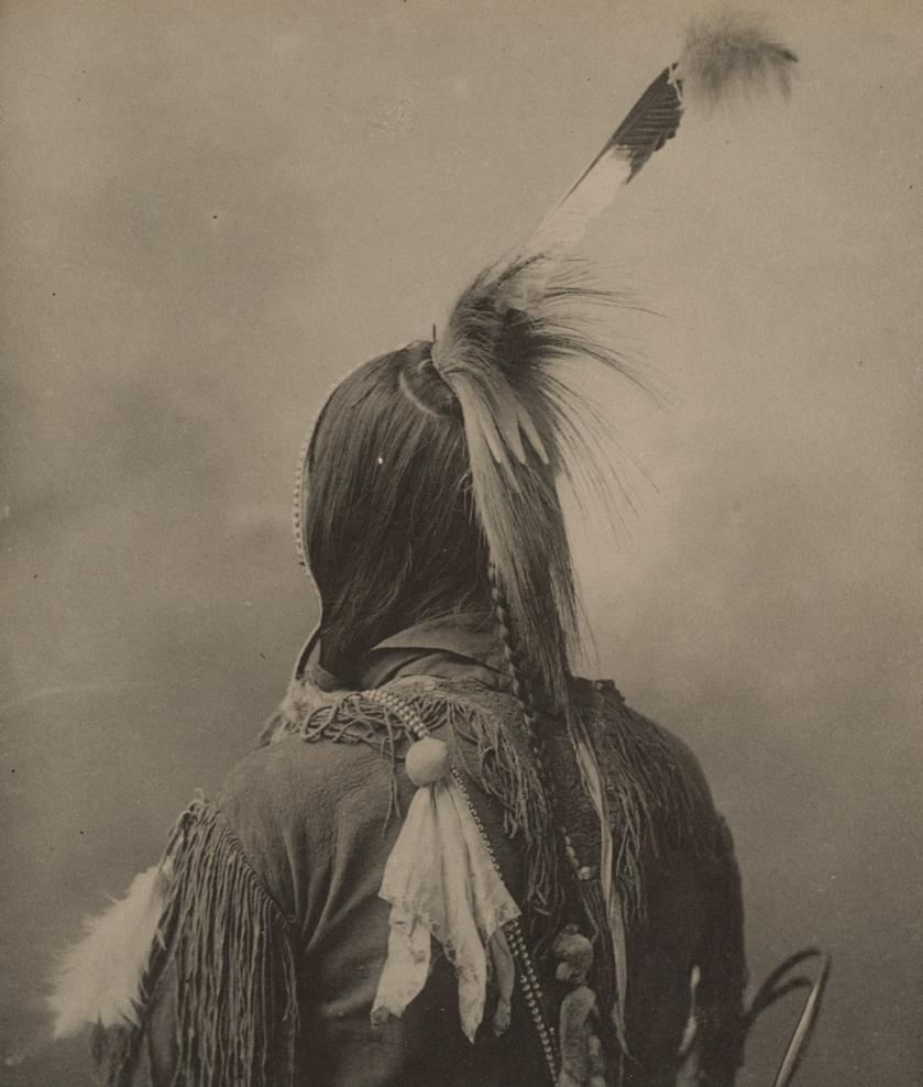A greyscale photograph of a Native American with their back to the camera