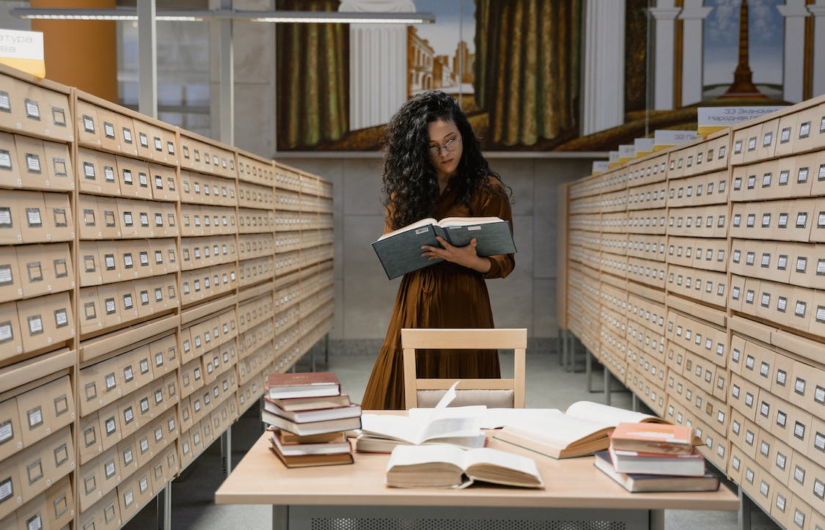 A person standing between archive drawers and reading from a book