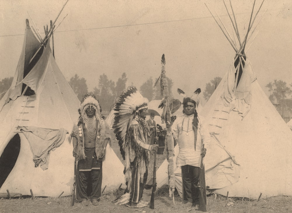 A photo of Native American standing near their tents 