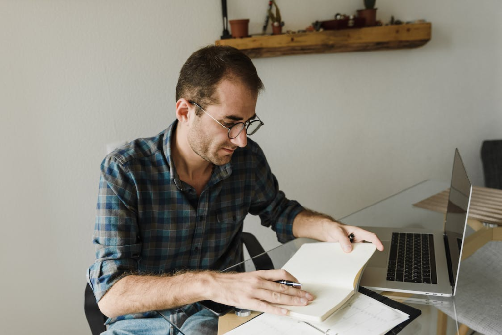 A person writing in a notebook with a laptop nearby