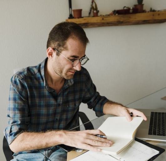 A person writing in a notebook with a laptop nearby