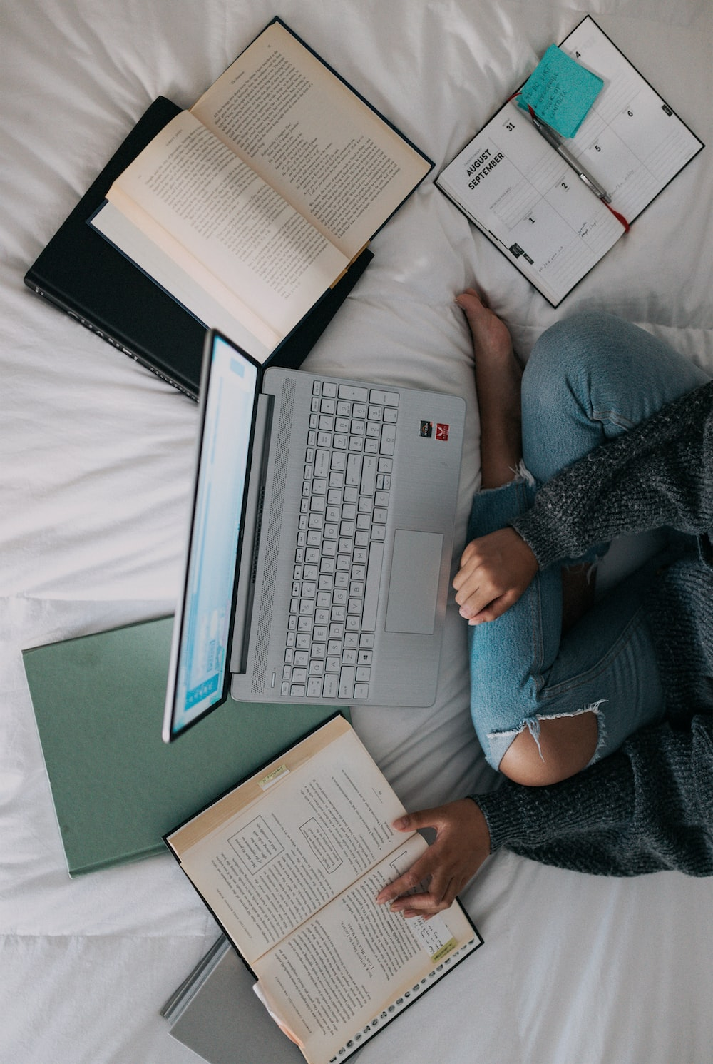 A person working on a laptop with open books nearby
