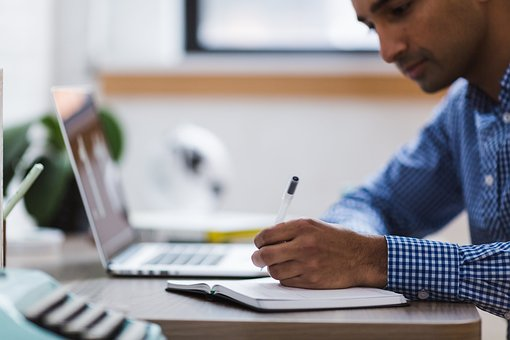  A person writing in a notebook with a laptop nearby