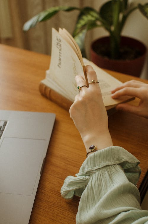 A person checking an old book placed near a laptop