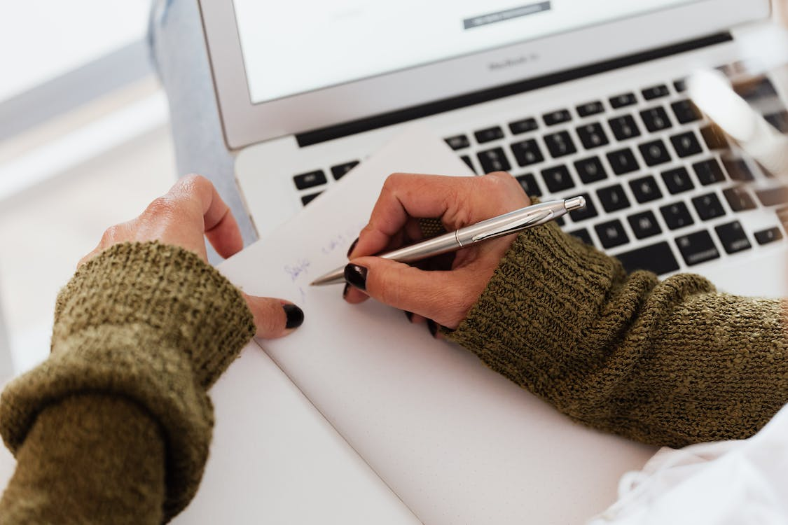 A person taking notes while working on a laptop