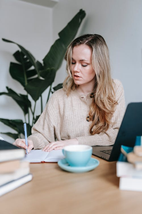 A person writing in a notebook with a laptop open in front of them 